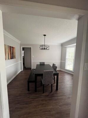 Un comedor con mesa y sillas de madera oscura, una l ámpara colgante y vista a un pasillo.