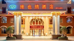 A hotel entrance with a prominent sign, large columns, and a well-lit facade. - Vienna Hotel (Shanghai)