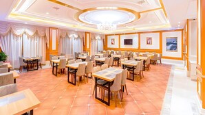 A spacious dining area with multiple tables and chairs, a chandelier, and artwork on the walls. - Vienna Hotel (Shanghai)