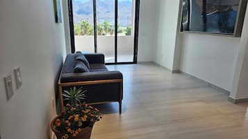 A modern living room with a sofa, a potted plant, and a view of mountains through large windows.