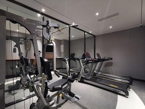 A gym with exercise equipment, treadmills, and a mirrored wall.