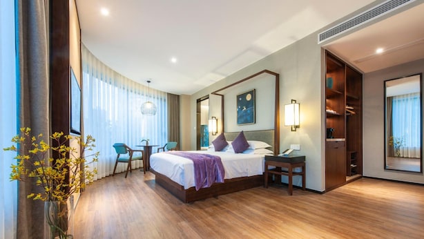 A hotel room with a bed, bedside table, a desk with a chair, a large window with curtains, a mirror, and a wall-mounted artwork. - Ssaw Boutique Hotel Cheng Man (Shanghai)