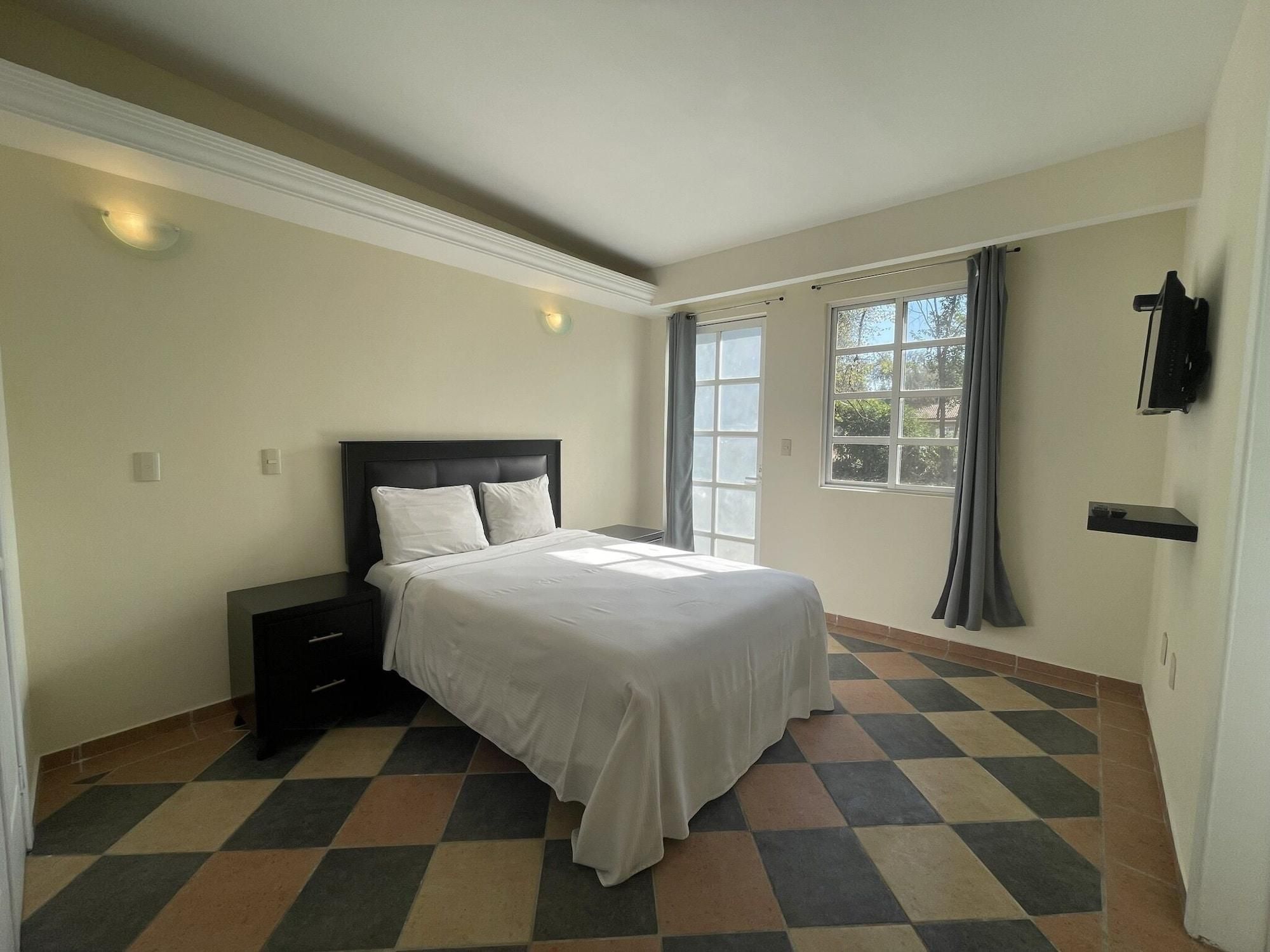 Un dormitorio con cama, mesita de noche y ventana con cortinas.