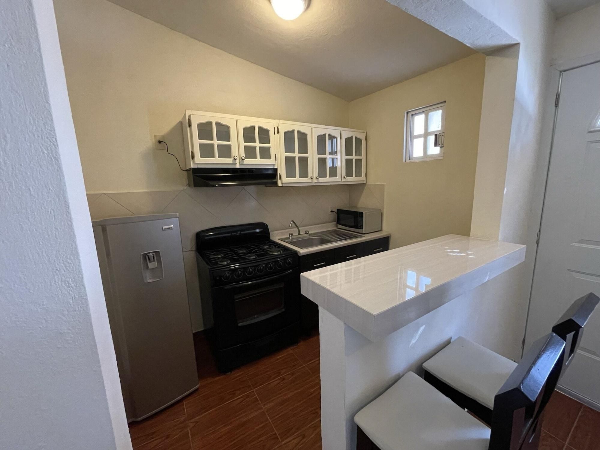 Una cocina compacta con refrigerador, estufa, microondas y gabinetes blancos.
