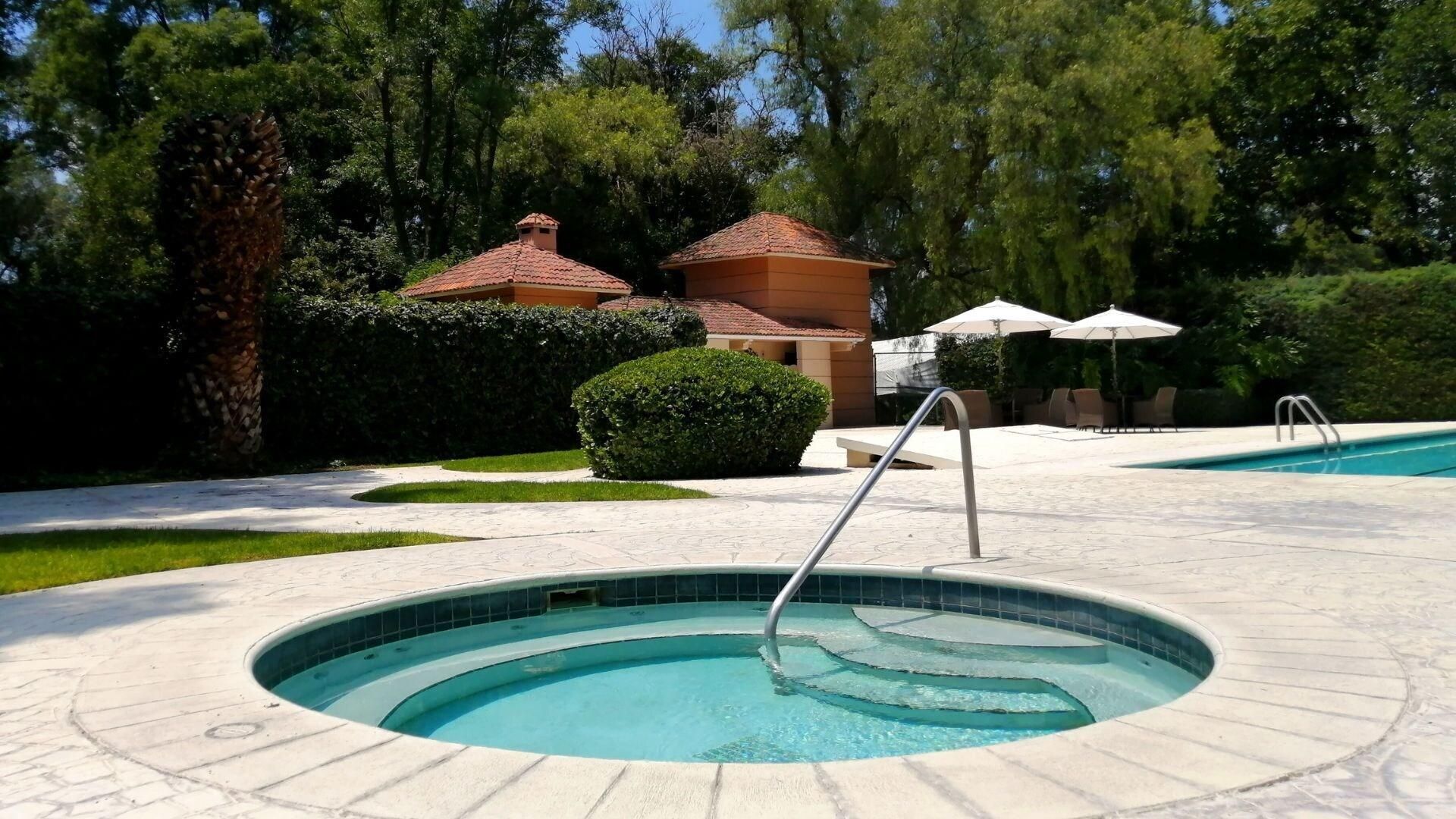 A circular pool with a metal ladder, surrounded by a paved area with chairs and umbrellas.