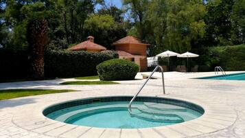 A circular pool with a metal ladder, surrounded by a paved area with chairs and umbrellas.