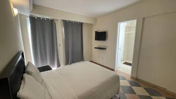 Una habitación de hotel con cama, cortinas, televisor de pantalla plana y puerta que da a un baño.