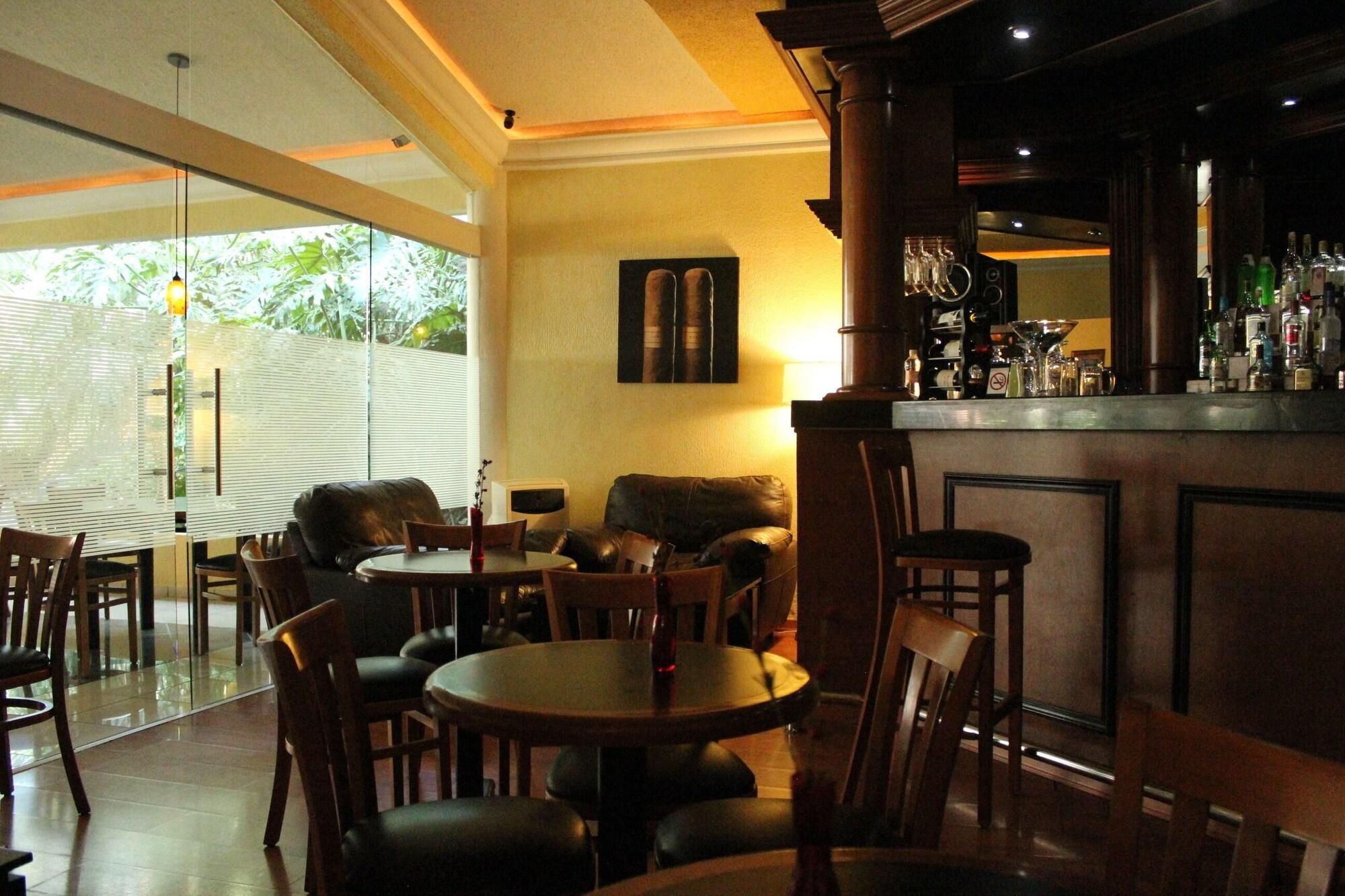 Zona de bar con barra, sillas y mesas. Hay un sofá y una mesa de comedor con sillas.