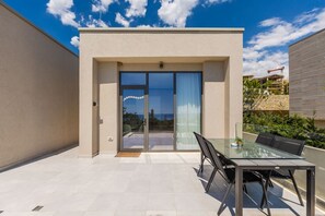 A modern building with a glass door entrance, a patio with a glass table and chairs, and a view of the sea. - Sapphire Coast Drymades Modern 2BR Apartment (Himarë)