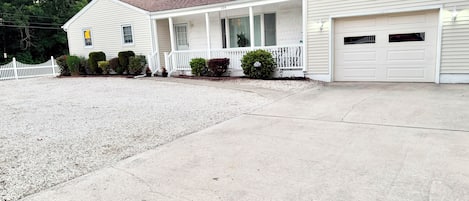 A single-story house with a front porch, a garage, and a gravel driveway.
