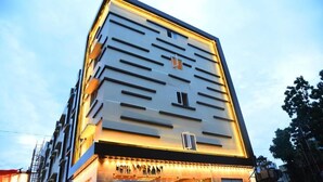 A hotel with a modern facade, multiple balconies, and a prominent entrance with illuminated signage. - Mango Hotels Vybrant Vijayawada by Othpl (Vijayawada)