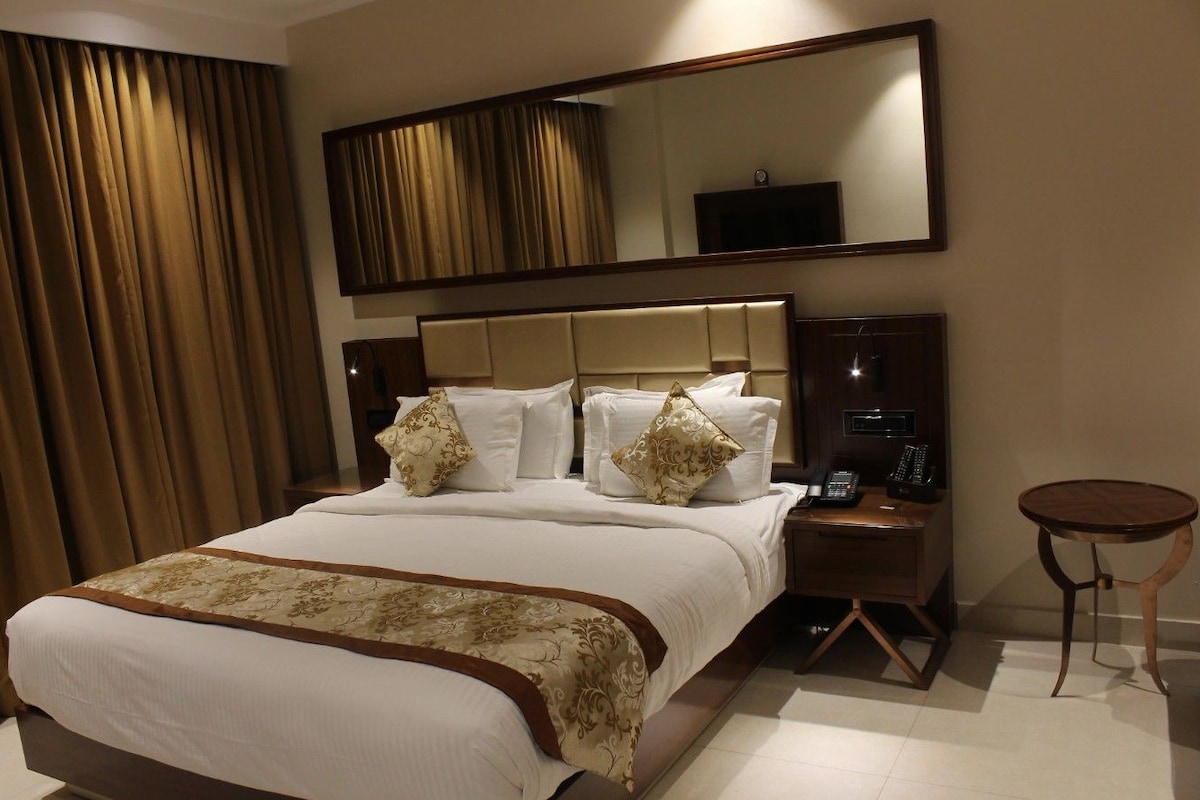 Habitación de hotel con una cama grande, una mesita de noche con lámpara, una pequeña mesa redonda y un espejo sobre la cama.