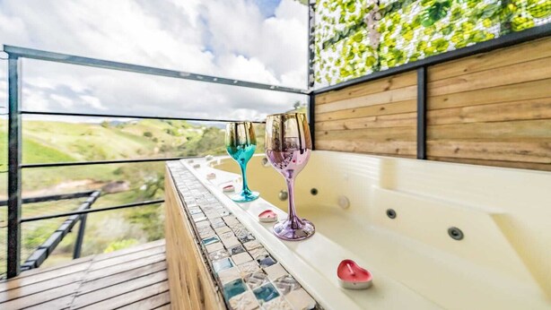 Un balcon donnant sur un espace verdoyant, une baignoire et deux verres.
