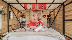 Une chambre à coucher chaleureuse et rustique, avec un plafond en bois, un lit agrémenté de touches de rouge et un décor en forme de cœur sur le mur.