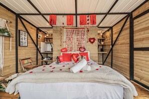 Ein gemütliches, rustikales Schlafzimmer mit Holzbalkendecke, einem Bett mit roten Akzenten und einer herzförmigen Dekoration an der Wand.