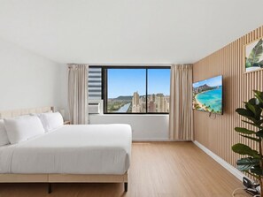 Habitación de hotel con una cama grande, un televisor en la pared y vistas de la ciudad a través de una ventana.
