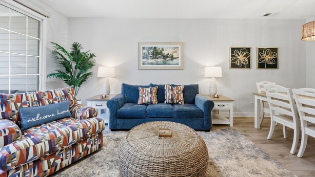 Een woonkamer met een bank, een salontafel, een eettafel met stoelen, een lamp en een plant.