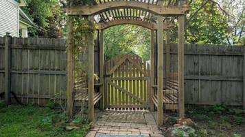 A wooden gate with a metal latch, surrounded by a wooden fence, and a paved pathway leading to it.