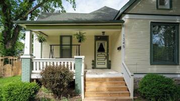 A two-story house with a front porch, a small front yard, and a wooden fence.
