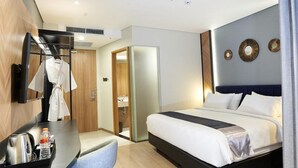 Et moderne hotelværelse med en seng, et skrivebord med elkedel og vandflaske, en badekåbe på stativ og et spejl på væggen.