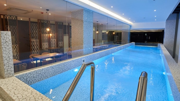 En indendørs swimmingpool med krystalklart, blåt vand, omgivet af et moderne interiør med glasvægge og stenelementer.