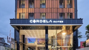 Et hotel med flere etager og en moderne facade, med en tydelig logo øverst og et skilt med 'CORDELA SUITES' i stueplan.