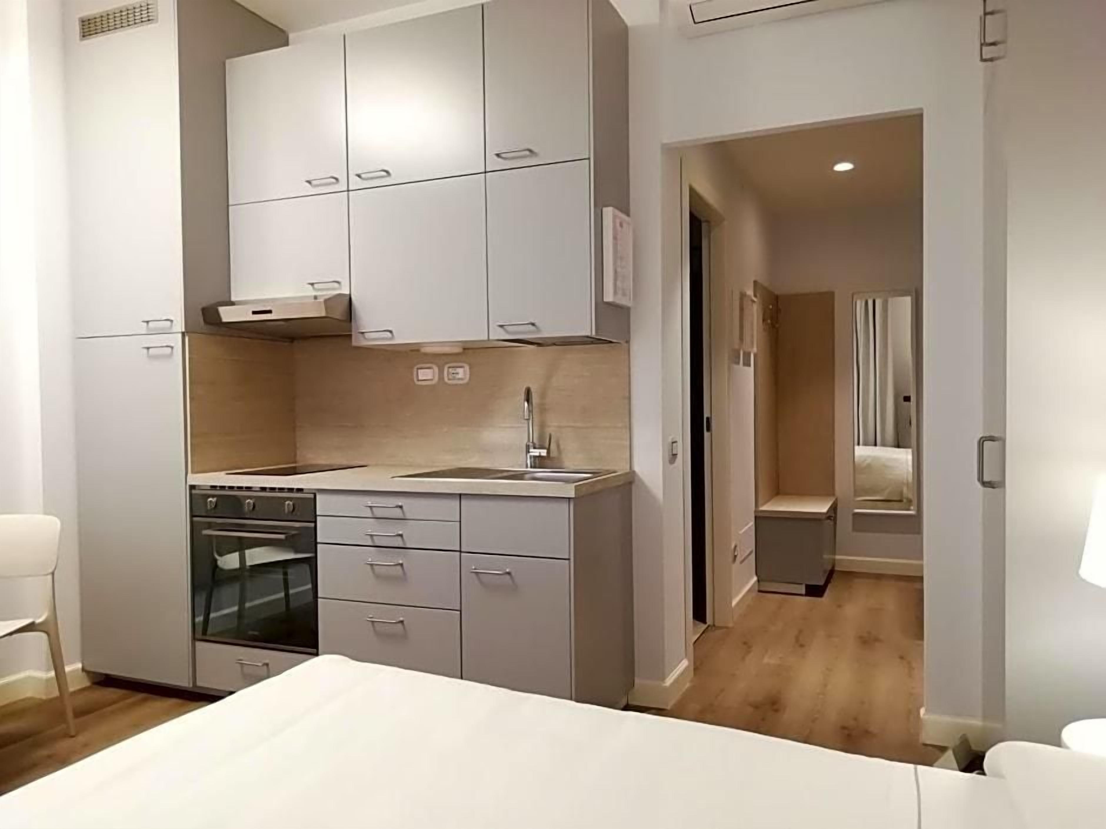 A modern kitchen with built-in appliances, a dining area with a white table, and a separate bedroom with a bed and nightstand.