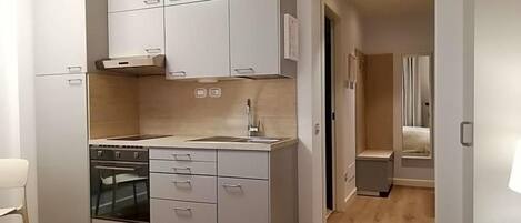 Una cocina moderna con electrodomésticos integrados, un comedor con mesa blanca y un dormitorio independiente con cama y mesita de noche.