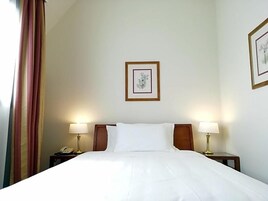 Una habitación de hotel con cama, dos lámparas de noche, un teléfono y un cuadro en la pared.