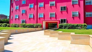 A multi-story building with a red facade, a central entrance, and a landscaped courtyard with steps leading to the entrance. - Delta Hotel (San Donato Milanese)