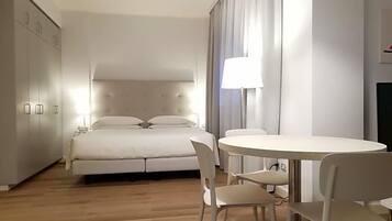 Un dormitorio con cama, mesita de noche, lámpara y un comedor con sillas.