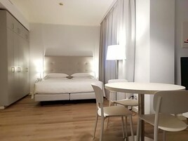Un dormitorio con cama, mesita de noche, lámpara y un comedor con sillas.