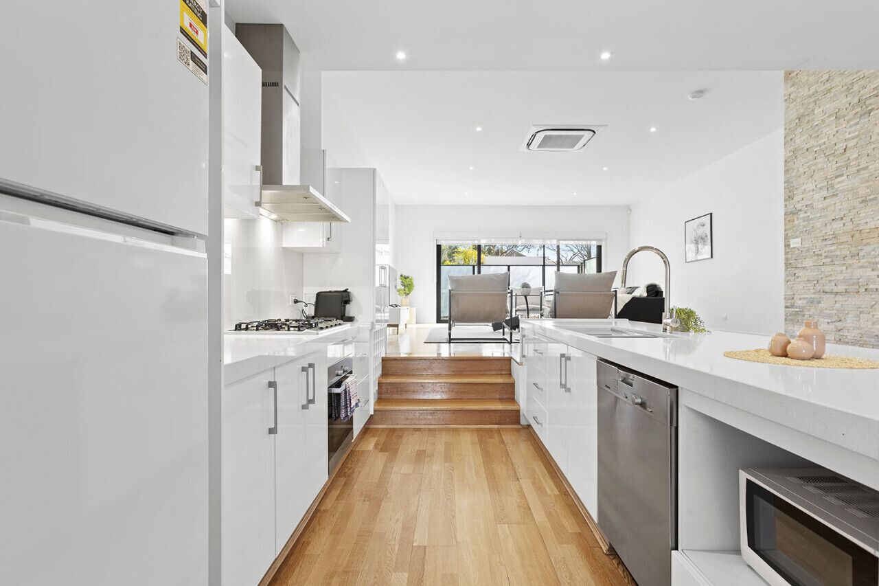 A modern kitchen with white cabinetry, a built-in oven, and a stone accent wall.