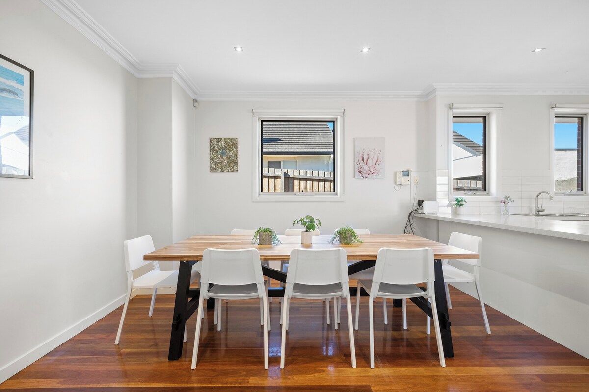 Un comedor moderno con una mesa de madera y sillas blancas, una ventana con vistas y un salpicadero blanco de azulejos.