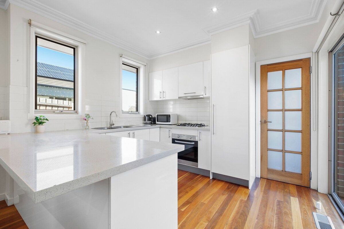 A modern kitchen with white cabinetry, a central island, and a view of the outside through a window.