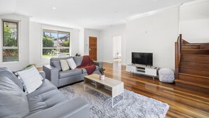 Ein modernes Wohnzimmer mit grauem Sofa, einem Couchtisch, einem Flachbildfernseher und einer Treppe.