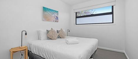 Un dormitorio con cama, mesita de noche, lámpara, ventana y un cuadro en la pared.