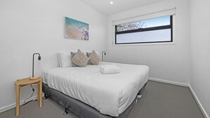 Ein Schlafzimmer mit einem Bett, einem Nachttisch, einem Fenster und einem Gemälde an der Wand.