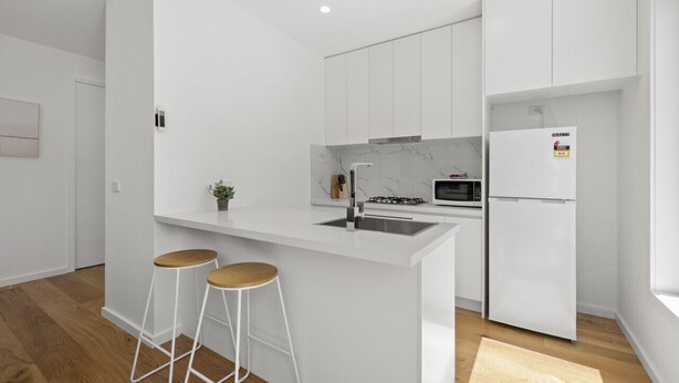 Eine moderne Küche mit weißen Schränken, einer zentralen Kochinsel mit Barhocker, einer Mikrowelle und einem Kühlschrank.