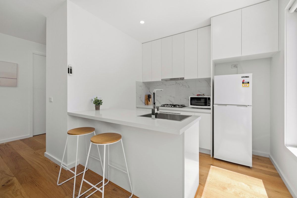 A modern kitchen with white cabinetry, a central island with stools, a built-in microwave, and a refrigerator.