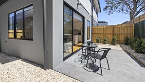 Ein modernes Haus mit Terrasse, einem Esstisch und Stühlen sowie einem Holzzaun.