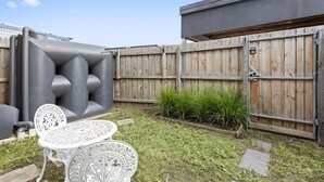 Un jardin avec une table et des chaises en métal, une clôture en bois et un portail en métal.
