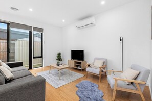 A modern living room with a grey sofa, a wooden coffee table, a TV stand, and a grey armchair.