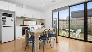 Une cuisine moderne avec des armoires blanches, un four à micro-ondes encastré et un coin repas comprenant une table et des chaises en bois.