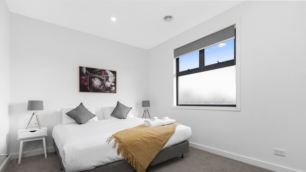 Une chambre moderne comprenant un lit, deux tables de chevet, une lampe sur pied, une fenêtre et une œuvre d’art accrochée au mur.