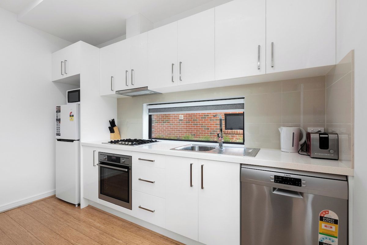 A modern kitchen with white cabinets, stainless steel appliances, and a brick wall view.