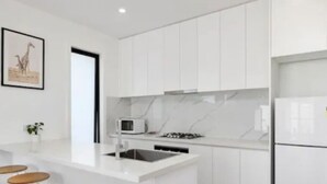 A modern kitchen with white cabinetry, a marble countertop, a microwave, and a refrigerator.