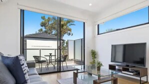 A modern living room with a sofa, a glass coffee table, a flat-screen TV, and a sliding glass door leading to an outdoor patio.