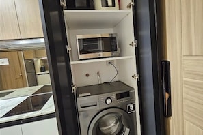 A compact kitchen with a microwave and a washing machine. - Luxury condo with gym,WiFi,NETFLIX at Park Mckinley West, Venice, SM Aura BGC (Taguig)