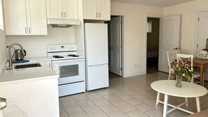 Una cocina moderna con armarios blancos, horno empotrado, refrigerador de acero inoxidable y una pequeña mesa de comedor con un florero.
